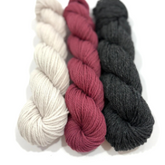 Three skeins of twisted yarn arranged vertically on a white background, in cream, dusty rose, and charcoal gray.