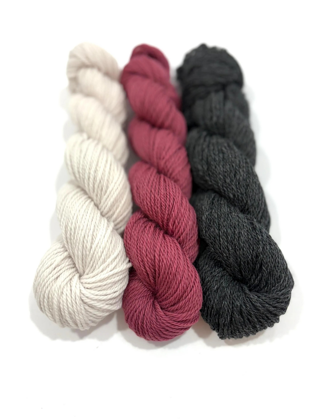 Three skeins of twisted yarn arranged vertically on a white background, in cream, dusty rose, and charcoal gray.