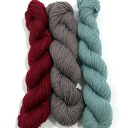 Three skeins of twisted yarn in burgundy red, charcoal gray, and dusty sage green, arranged vertically on a white background.