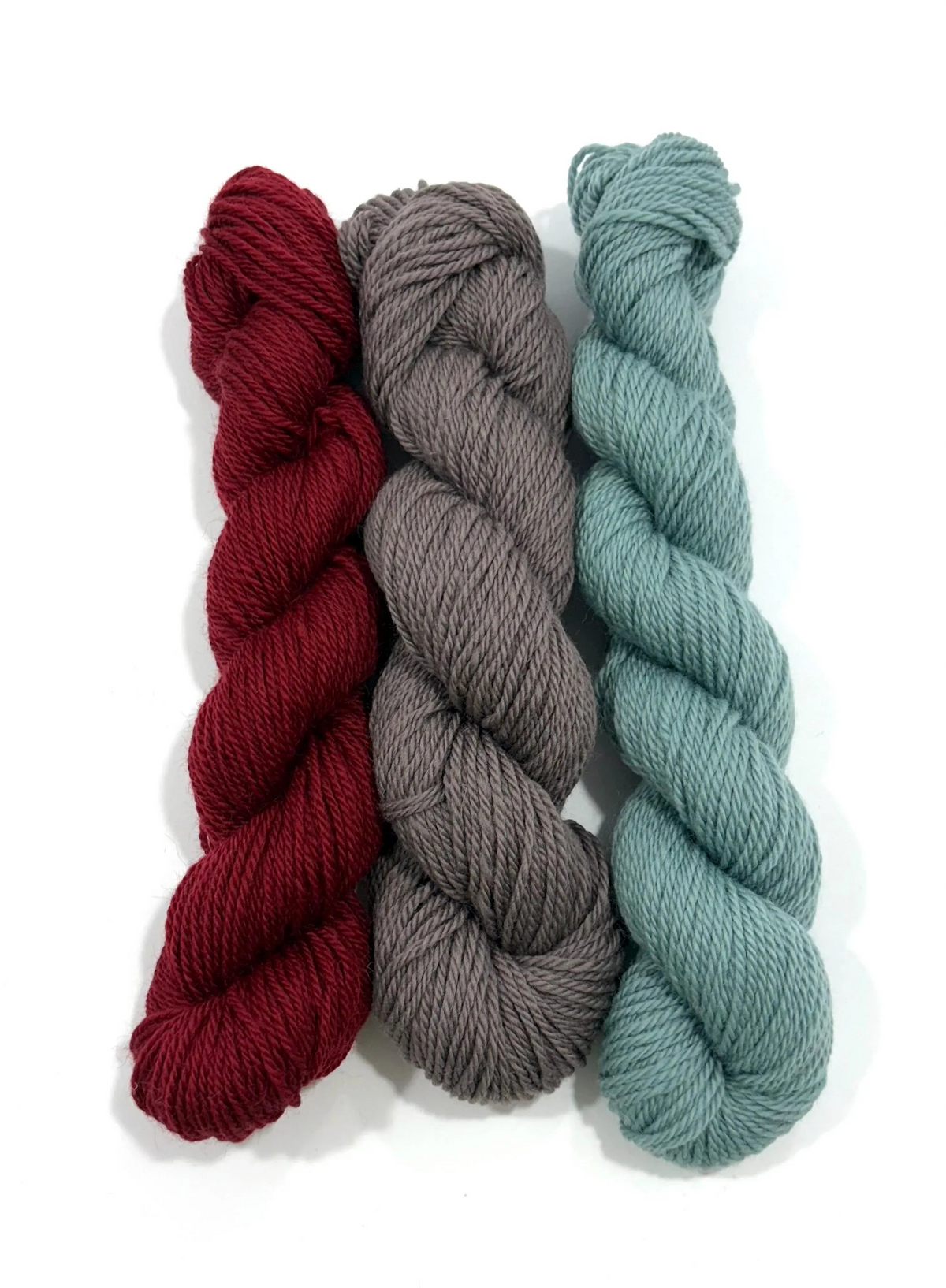 Three skeins of twisted yarn in burgundy red, charcoal gray, and dusty sage green, arranged vertically on a white background.
