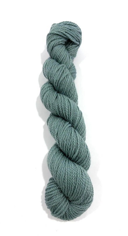 A single skein of twisted yarn in a muted sage green color, photographed vertically against a plain white background.