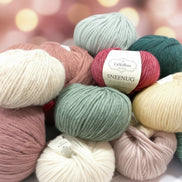 Snefnug By CaMaRose Merino Alpaca Cotton Airy and Plump Yarn Worsted Weight Super Soft Yarn Perfect for Cardigans and Sweaters. A pile of colorful yarn skeins in cream, navy, pink, green, yellow, purple, and light blue, with a central label reading 'CraMaRose SNEFNUG'.