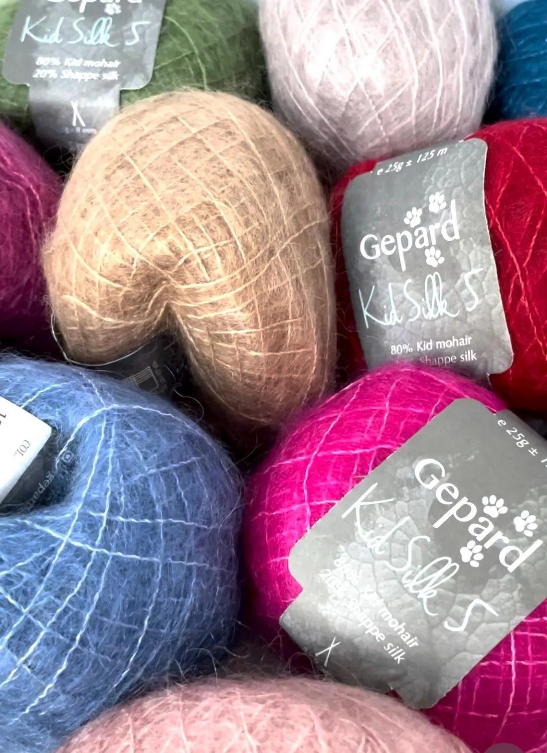A close-up pile of colorful yarn balls with gray Gepard Kils Silk 5 labels, including pink, blue, beige, red, green, and lavender shades.