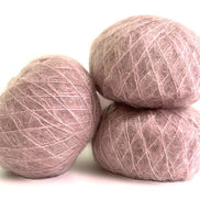 Three balls of dusty pink wool yarn stacked together on a white background.