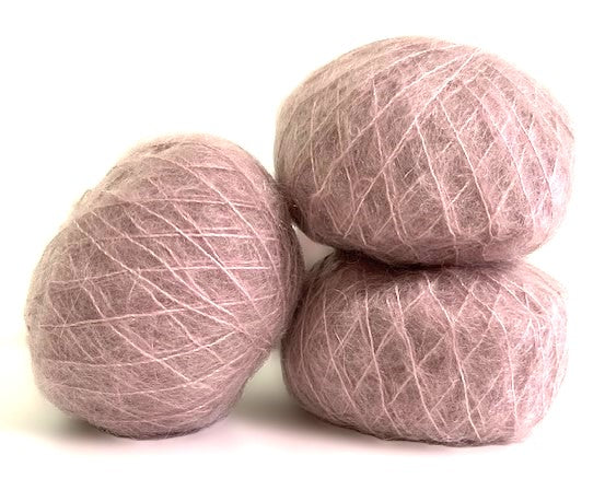 Three balls of dusty pink wool yarn stacked together on a white background.