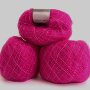 Three balls of bright magenta pink yarn stacked together on a light gray background. The top ball has a silver paper label wrapped around it.