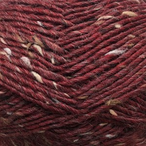 Close-up of a variegated yarn skein in a deep burgundy red color, featuring small flecks of off-white and light tan yarn throughout.