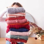 Person holding a stack of colorful sweaters in front of a white wall.