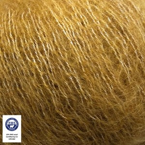 A close-up of fluffy golden-brown hair or fiber strands, with a small certification label in the lower-left corner.