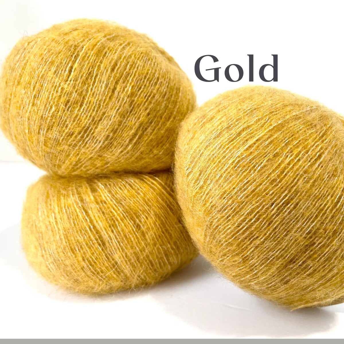 Three balls of fuzzy yarn in a warm golden yellow color, stacked on a white background with the word 'Gold' printed in black text.