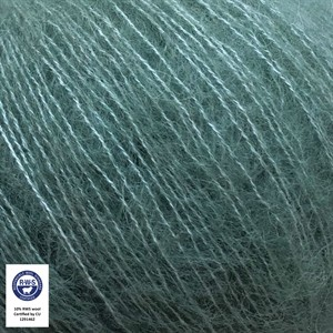 Close-up of a ball of dusty teal-green yarn with fine strands visible, featuring a small white certification label in the bottom-left corner.