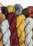 A row of twisted yarn skeins in multiple colors, including black, gray, beige, orange, burgundy, yellow, blue, olive green, and mauve, arranged against a plain white background.